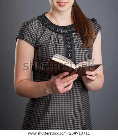 Unrecognizable young woman holding an opened book, grey background