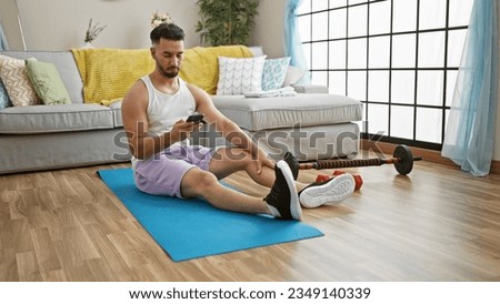 Young arab man sitting on yoga mat using smartphone at home