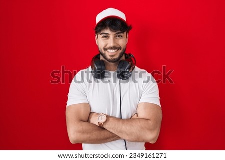 Hispanic man with beard wearing gamer hat and headphones happy face smiling with crossed arms looking at the camera. positive person. 