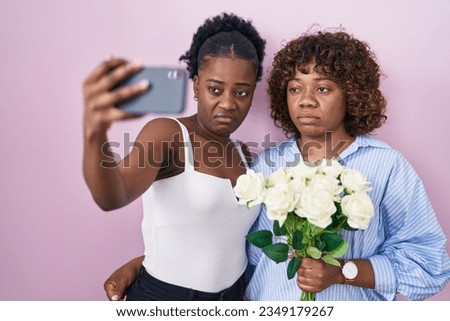 Two african women taking a selfie photo with flowers skeptic and nervous, frowning upset because of problem. negative person. 
