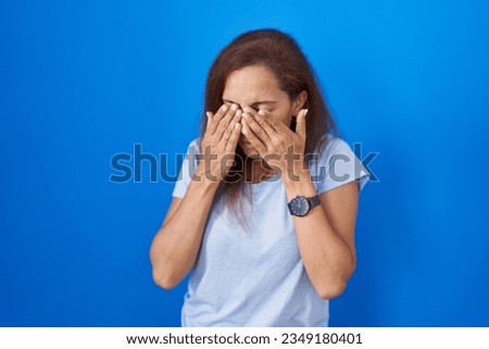 Brunette woman standing over blue background rubbing eyes for fatigue and headache, sleepy and tired expression. vision problem 