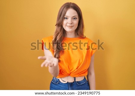 Caucasian woman standing over yellow background smiling cheerful offering palm hand giving assistance and acceptance. 
