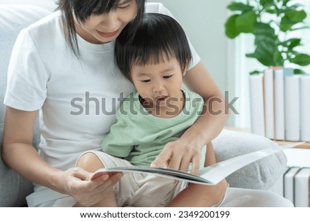 Happy Asian mother relax and read book with baby time together at home. parent sit on sofa with daughter and reading a story. learn development, childcare, laughing, education, storytelling, practice.