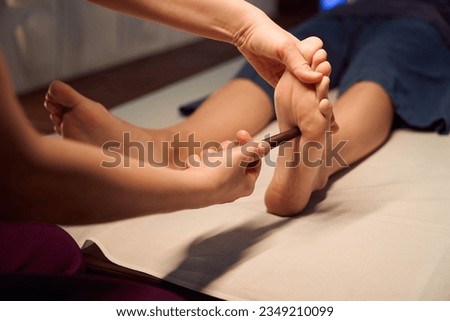 Experienced reflexologist stimulating acupoint on patient sole with massage tool
