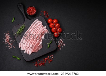 Fresh raw bacon cut into slices with salt, spices and herbs on a dark textured concrete background Royalty-Free Stock Photo #2349213703