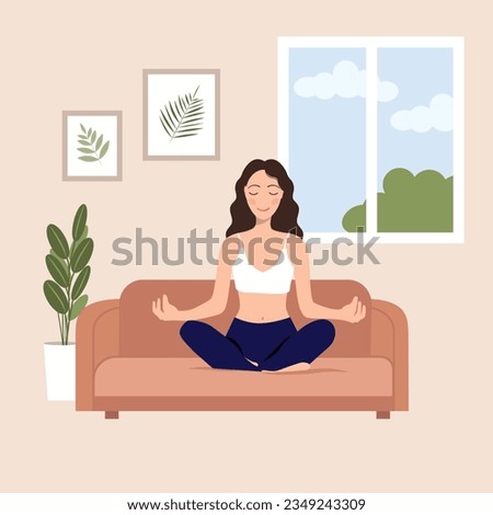 yoga at home. the girl sits at home on the couch and meditates against the background of the window and paintings. Breathing practices, yoga, meditation concept
