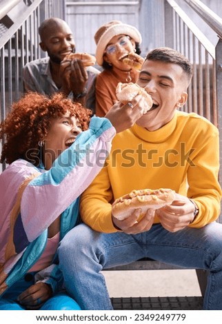 Friends, city and feeding food outdoor for happiness, funny laugh and fun on stairs. Diversity, eating and gen z group of men and women with a hotdog on a date, adventure and freedom in urban town Royalty-Free Stock Photo #2349249779