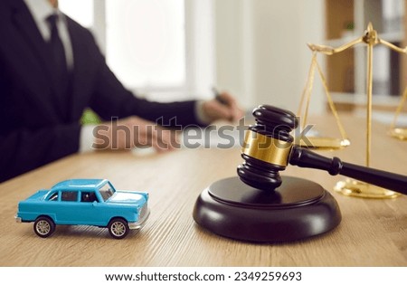 Small toy car and judge's gavel on table and against background of judge signing document. Concept of selling car by auction, accident sentence or car insurance. Close up.