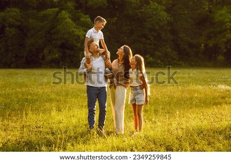 Happy family strolling in nature all together. Happy, joyful mother, father and little children walking on green grass in a beautiful park on a sunny summer evening Royalty-Free Stock Photo #2349259845