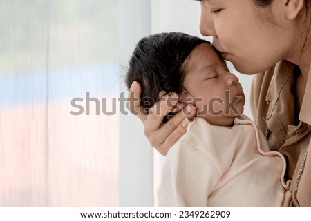 an Asian mother kissing forehead his 1-month-old baby newborn daughter, with happy and love, concept to Asian family and baby newborn