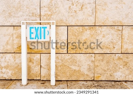 EXIT sign placed next to a wall constructed from sturdy stone slabs.