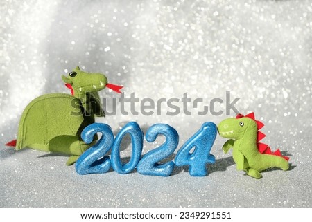 New Year 2024 holiday concept. festive decorative numbers 2024 and cute soft toy dragons close up on light silver shiny abstract glittering background. lunar new year symbol. element for design.