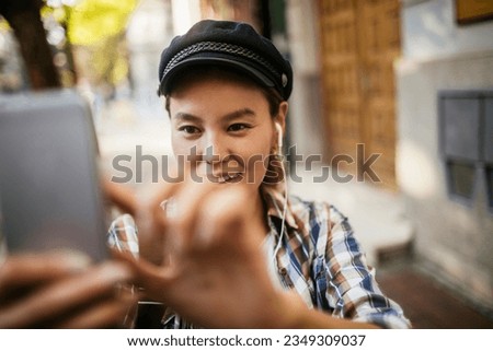 Young woman using her smart phone to take a picture while walking on a sidewalk in the city