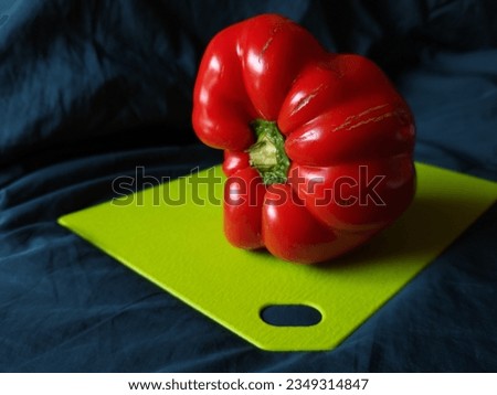 A sweet red pepper, flecked with signs of decay, lays gracefully on a green plastic tray. The bright red shade of the pepper harmoniously contrasts with the greens of the tray.