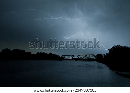 Lightning strikes with eerily beautiful gray forks through a dangerous sky above and beyond a turn-of-the-century iron truss train bridge over the Des Moines river.