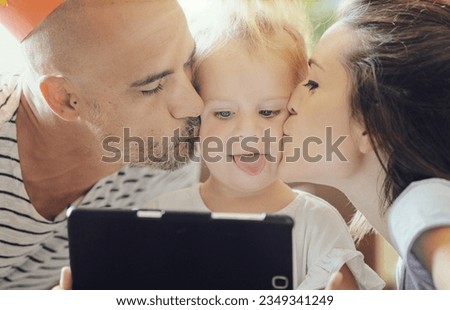 Close-up picture of two parents kissing their little girl on her cheeks while she plays with the tablet (she stucks her tongue out)