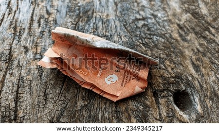 Scuffed 5000 rupiah note on wood texture. 