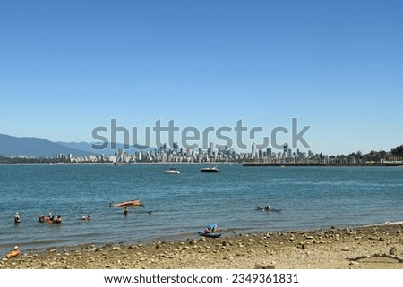 Shoreline of English Bay with swimmers, boaters and Vancouver skyline in background.