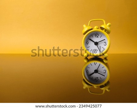 Yellow alarm clock on yellow background with reflection on a black acrylic board. Copy and text space.