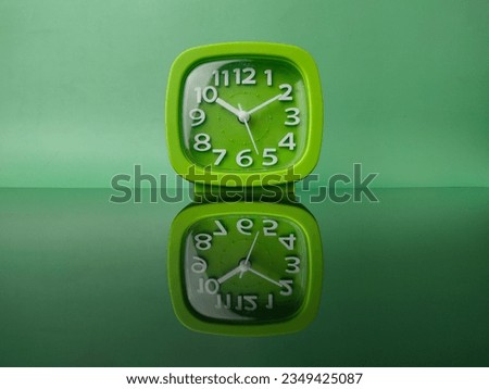 Green clock on green background with reflection on a black acrylic board