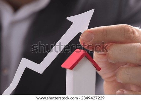 Businessman Holding Paper Graph Over The Increasing House Miniature