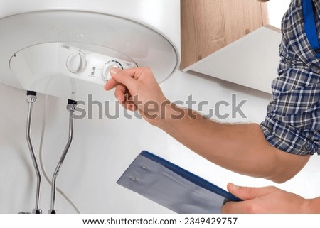 Male Worker With Clipboard Adjusting Temperature Of Water Heater Royalty-Free Stock Photo #2349429757