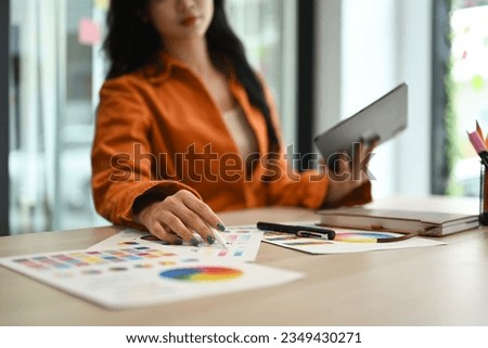 Select focus on woman hand choosing colors from color swatch samples and using digital tablet at workstation..