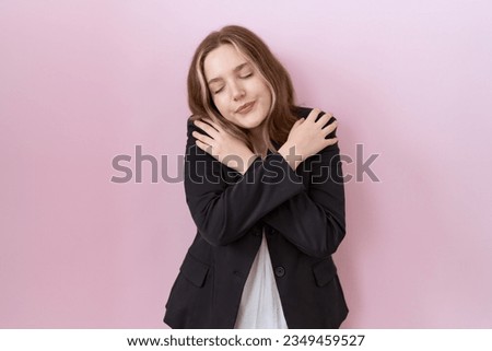 Young caucasian business woman wearing black jacket hugging oneself happy and positive, smiling confident. self love and self care 