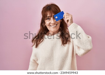 Middle age hispanic woman holding credit card covering eye looking positive and happy standing and smiling with a confident smile showing teeth 