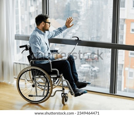 Portrait of a lonely depressed sad and worried young man in wheelchair using laptop by the window, person with chronic health condition, man with paraplegia Royalty-Free Stock Photo #2349464471