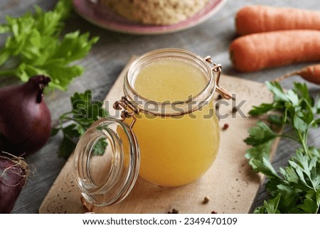 Bone broth or bouillon in a glass jar with fresh vegetables on a rustic table