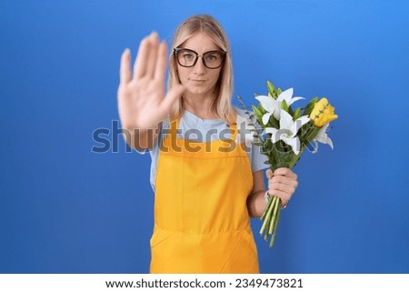 Young caucasian woman wearing florist apron holding flowers doing stop sing with palm of the hand. warning expression with negative and serious gesture on the face. 