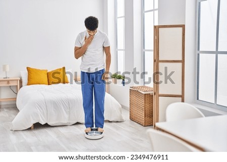 Arab man looking at weight machine to balance weight loss covering mouth with hand, shocked and afraid for mistake. surprised expression  Royalty-Free Stock Photo #2349476911