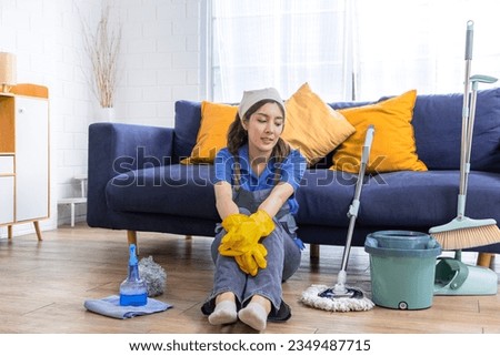 Portrait of stress Asian housekeeper female wearing gloves and apron get tired sitting on floor with mop cleaning equipment, housewife discouraged feeling with unfinished routine housework or boring
