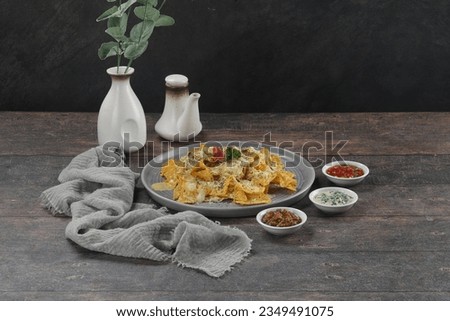Nachos chips with melted cheese and dips variety in grey plate. On wood background.