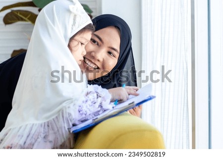 Muslim woman with Hijab teaching little girl with hijab. Traditional muslim family.  Islamic mother or teacher  smiling  and happy to teach girl to write.