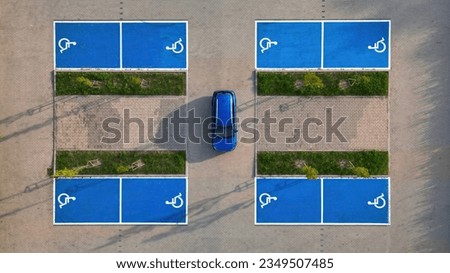 Outdoor car parking places with handicapped symbol icons, parking places reserved for disabled person, blue car between parking places - aerial drone top down view.