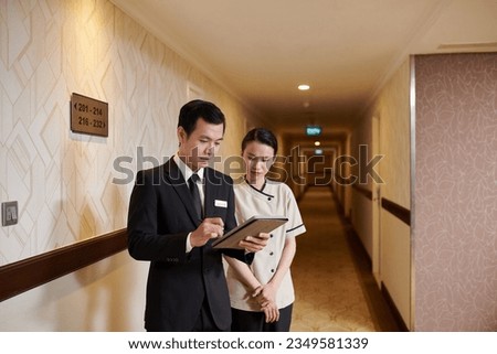 Manager and hotel maid checking list of guests on tablet computer before cleaning rooms Royalty-Free Stock Photo #2349581339