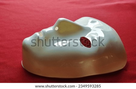 white plastic human face mask on red fabric background 