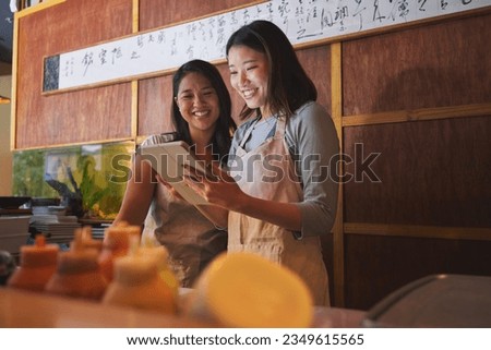 Cafe, tablet and asian women together at counter checking sales, booking or menu for small business. Social media, content marketing and startup restaurant owner with waitress scroll on digital app.