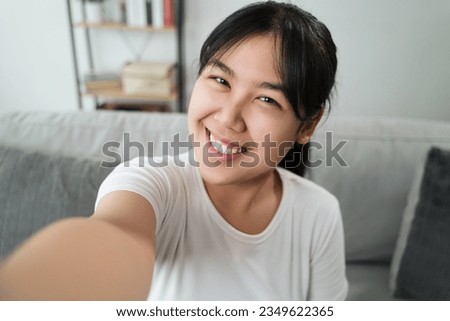 Young Asian Happy woman takes a selfie photo sitting on the sofa at home.