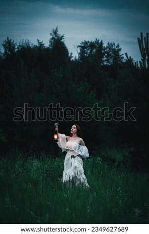 Lonely woman in a white dress with a kerosene lamp in her hands walks through the night field. The concept of fairy tale mysticism. Royalty-Free Stock Photo #2349627689