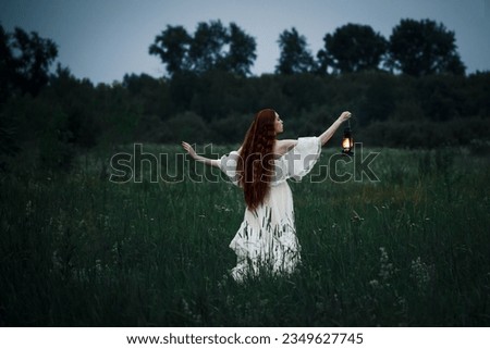 Lonely woman in a white dress with a kerosene lamp in her hands walks through the night field. The concept of fairy tale mysticism.