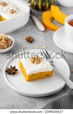 Spiced pumpkin cake with walnut and cream cheese frosting sliced into squares on a gray concrete background. Autumn dessert