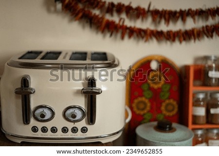 Vintage old fashion off white double quadruple slot toaster with dials and buttons that say "cancel" "reheat" "defrost" dried chillies hanging behind and spice rack shelf sunflower design ceramic jar Royalty-Free Stock Photo #2349652855