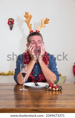 Christmas picture of boredom, as a man yawns whilst holding his head in his hands in an uninterested pose. An anti-Christmas image. Selective focus on the mans face.