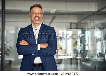 Handsome hispanic senior business man with crossed arms smiling aside. Indian or latin confident mature good looking middle age leader male businessman on blur office background with copy space. Royalty-Free Stock Photo #2349680477