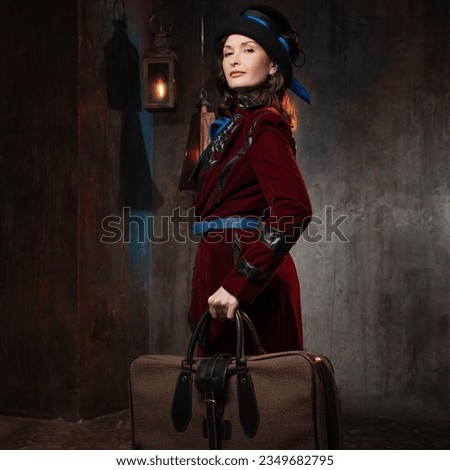 A stylish lady in a burgundy old-fashioned suit with a hat and a valise. Brunette in a retro style suit Royalty-Free Stock Photo #2349682795