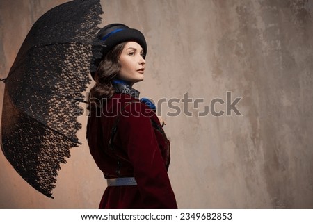 stylish lady in a burgundy old - fashioned suit with a hat and a lace umbrella . Brunette in a retro style suit Royalty-Free Stock Photo #2349682853