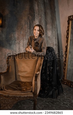 A stylish lady in an elegant Victorian-style suit, and armchair. costume with steampunk elements, Royalty-Free Stock Photo #2349682865